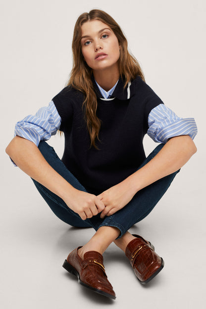 Navy sleeveless knit vest with crew neck and blue striped sleeves, seated