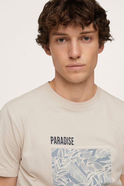 Men's sand T-shirt close-up with “PARADISE” and blue plant graphic