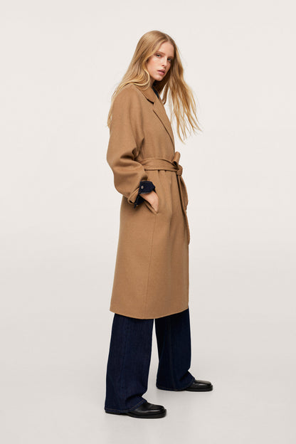 Tan long belted coat with lapels, side view, dark cuff trim and tied belt