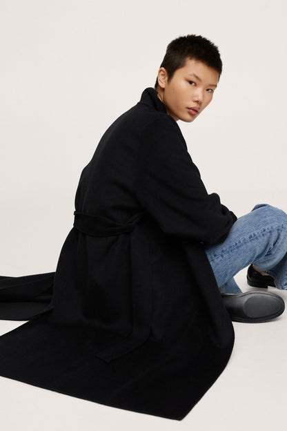Black long belted coat with wide sleeves and flowing hem, side angle