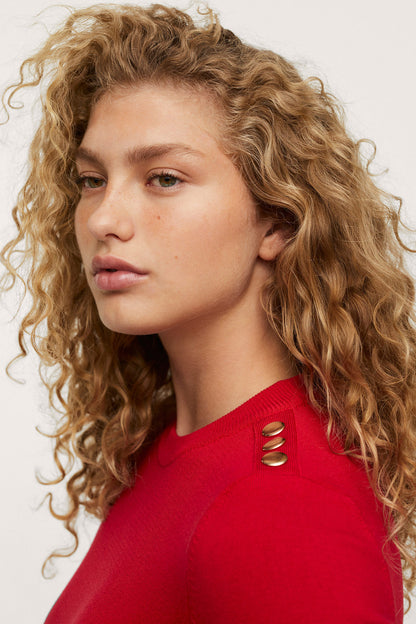 Red long-sleeve top with grommet cutout detail at the shoulder