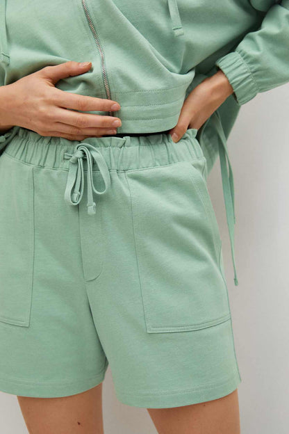 Pastel green hoodie hem and drawstring shorts with side pockets, close-up