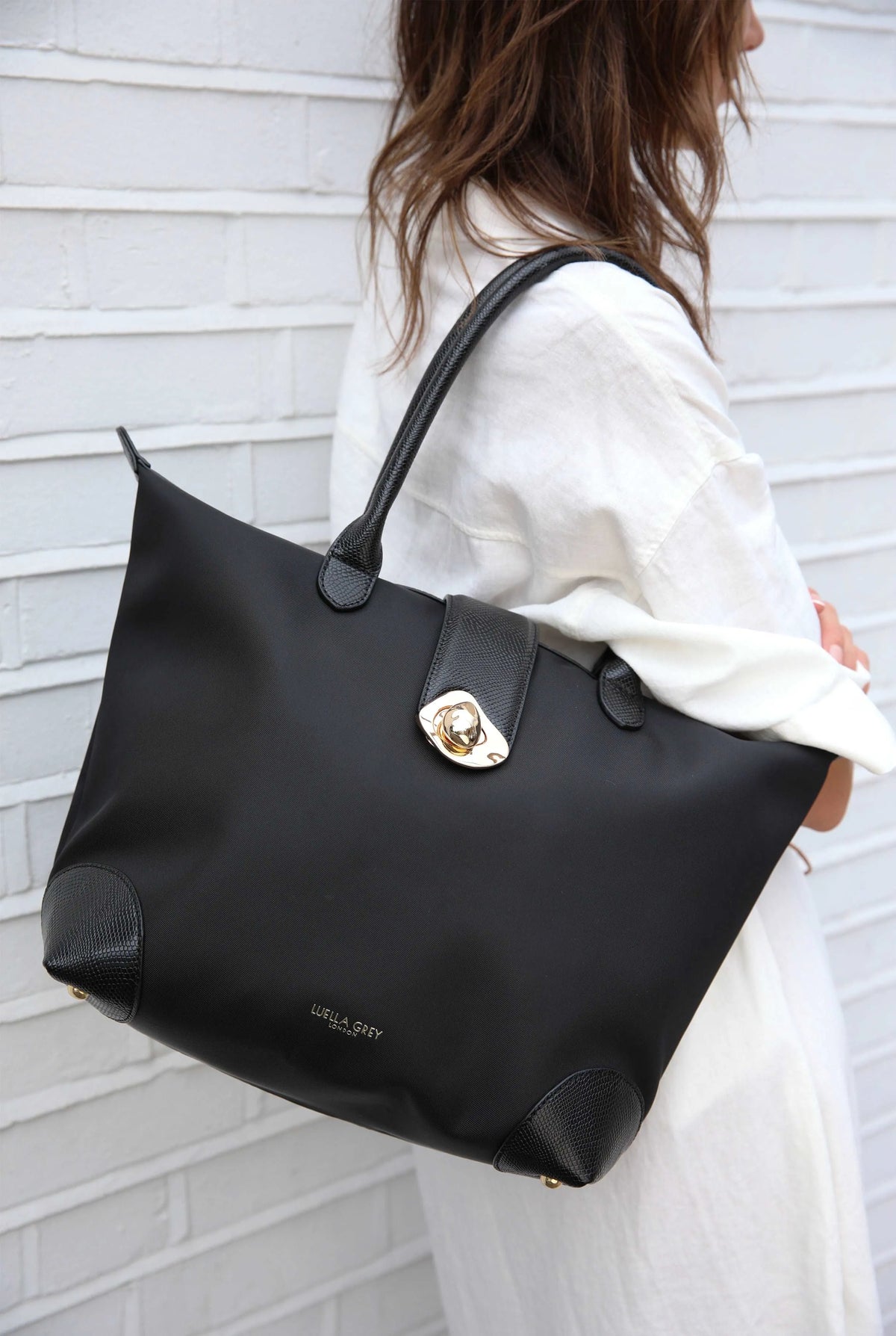 Black tote bag with gold clasp, side base, and smooth top handles