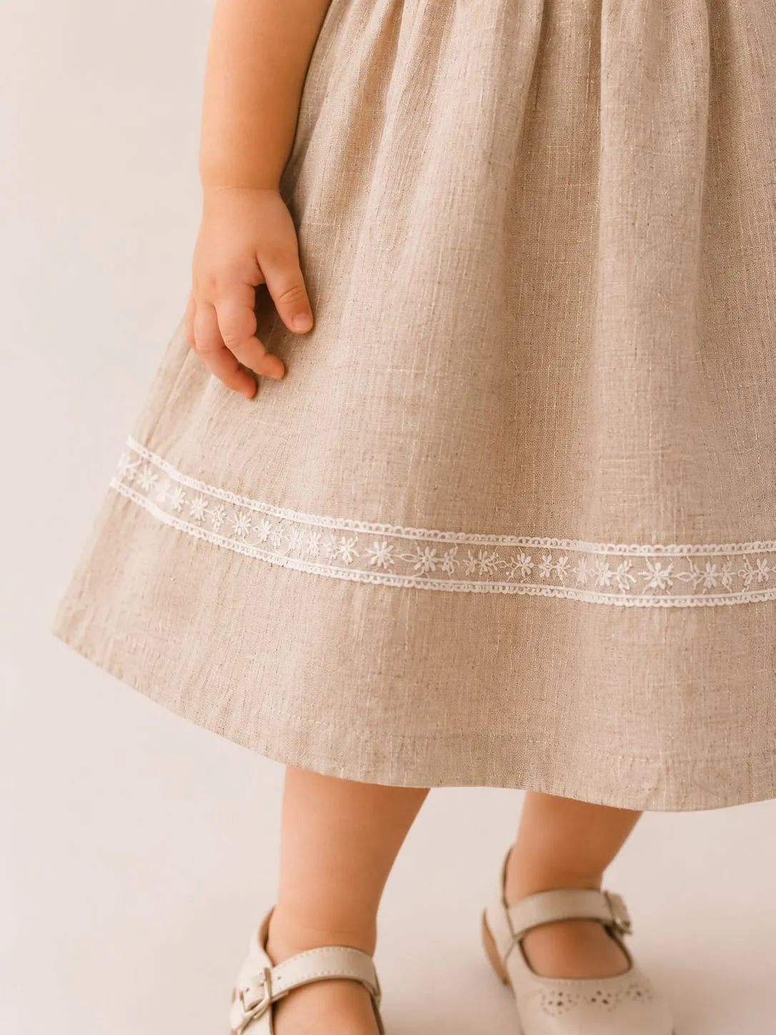 Stone linen dress hem with white stitched trim; flared skirt and sandals
