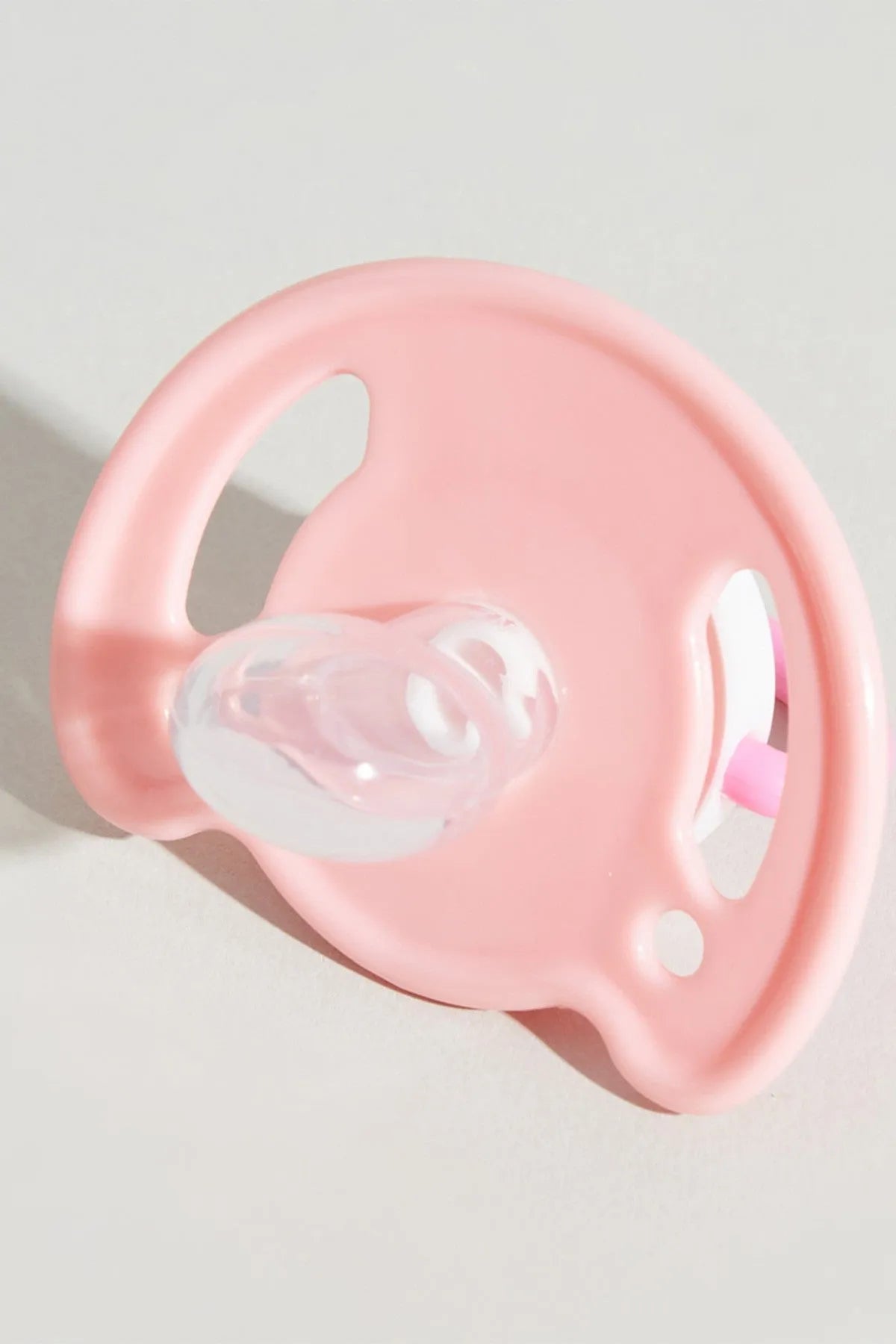 Pink pacifier with round shield and clear orthodontic nipple, side view