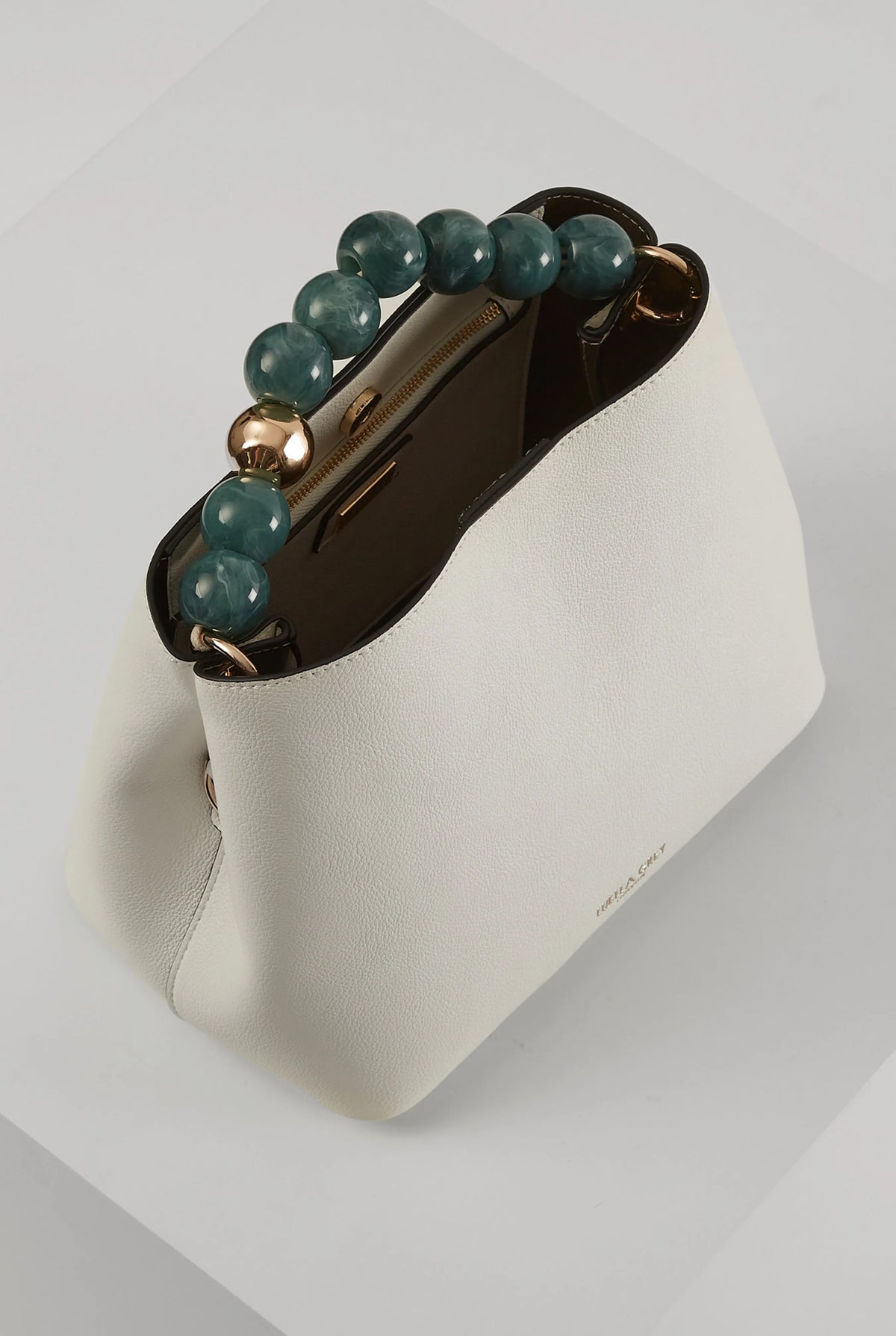 White bucket bag with green beaded handle, brown interior, and gold hardware clasp