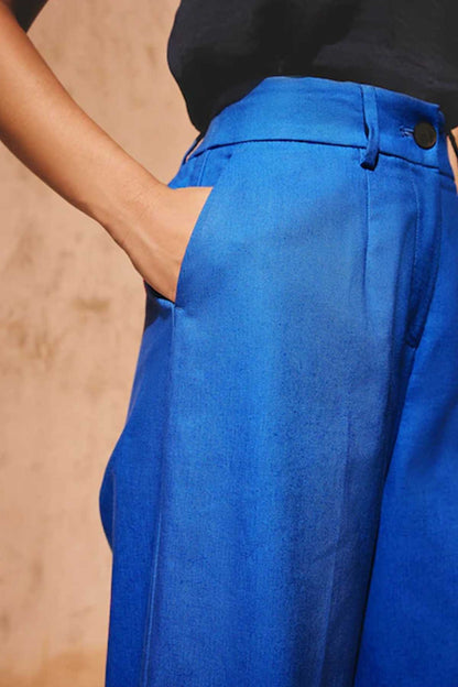 Women’s blue trousers close-up: front pleat, waistband seam, and button tab