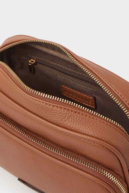 Tan leather-look crossbody bag close-up with dual zippers and logo patch