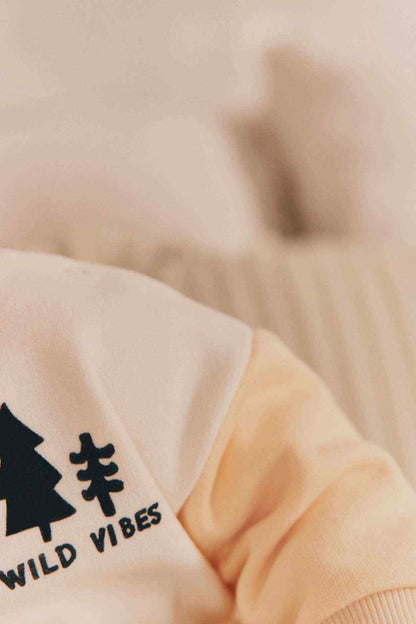 Cream long-sleeve top with Wild Vibes tree graphic and bold text, crew neckline