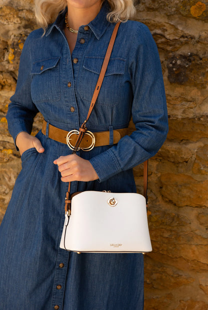 White crossbody handbag worn with tan strap, gold clasp front, and buckle accents