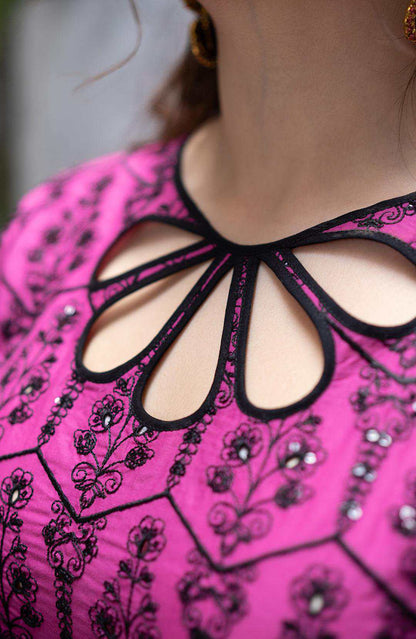 Close-up of magenta neckline with black cutout trim and intricate embroidery pattern