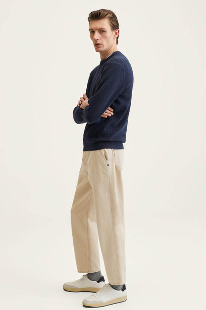 Navy crewneck sweater with long sleeves, side view, worn with beige trousers