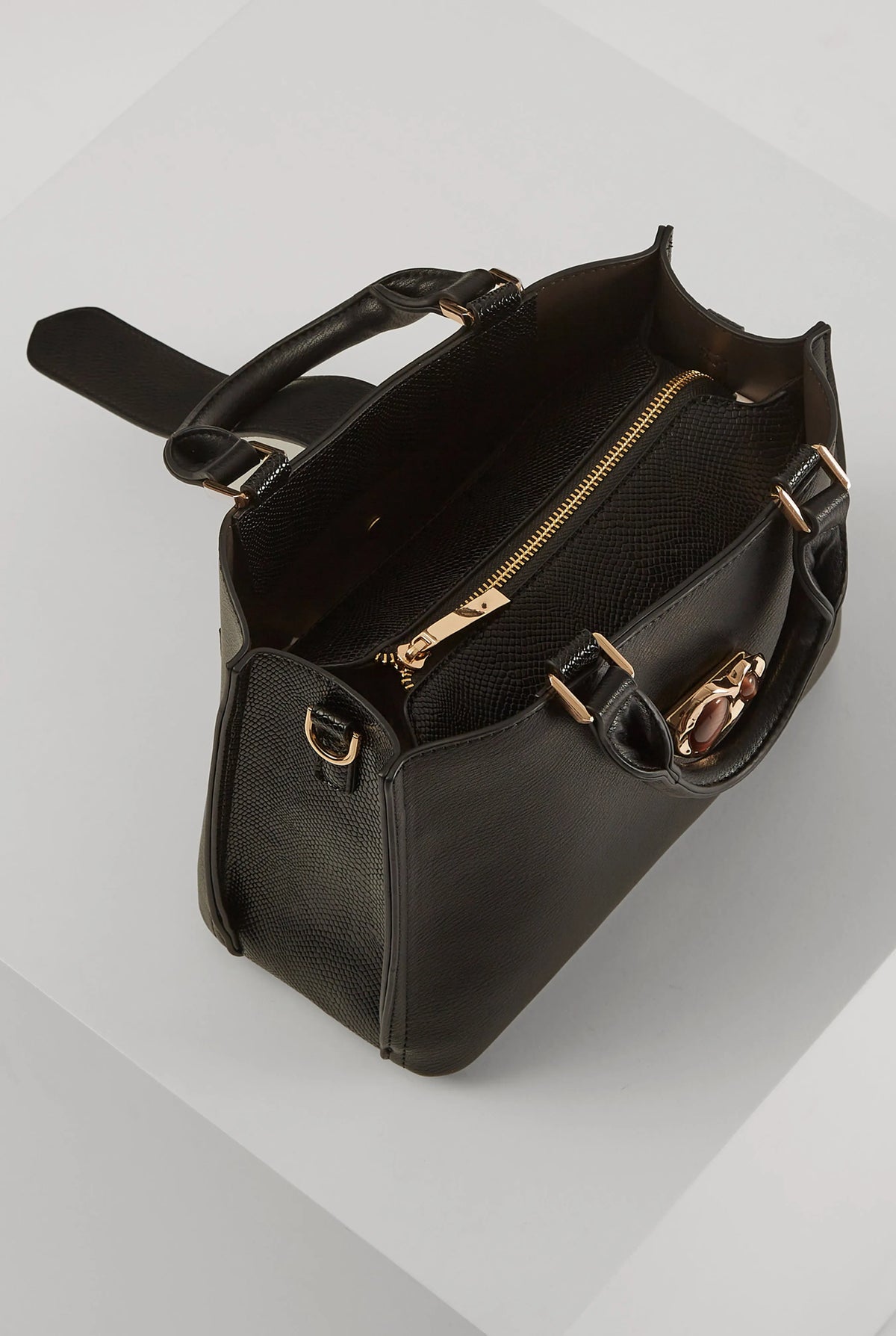 Black handbag with top handle, buckled side straps, and gold-tone zip compartment