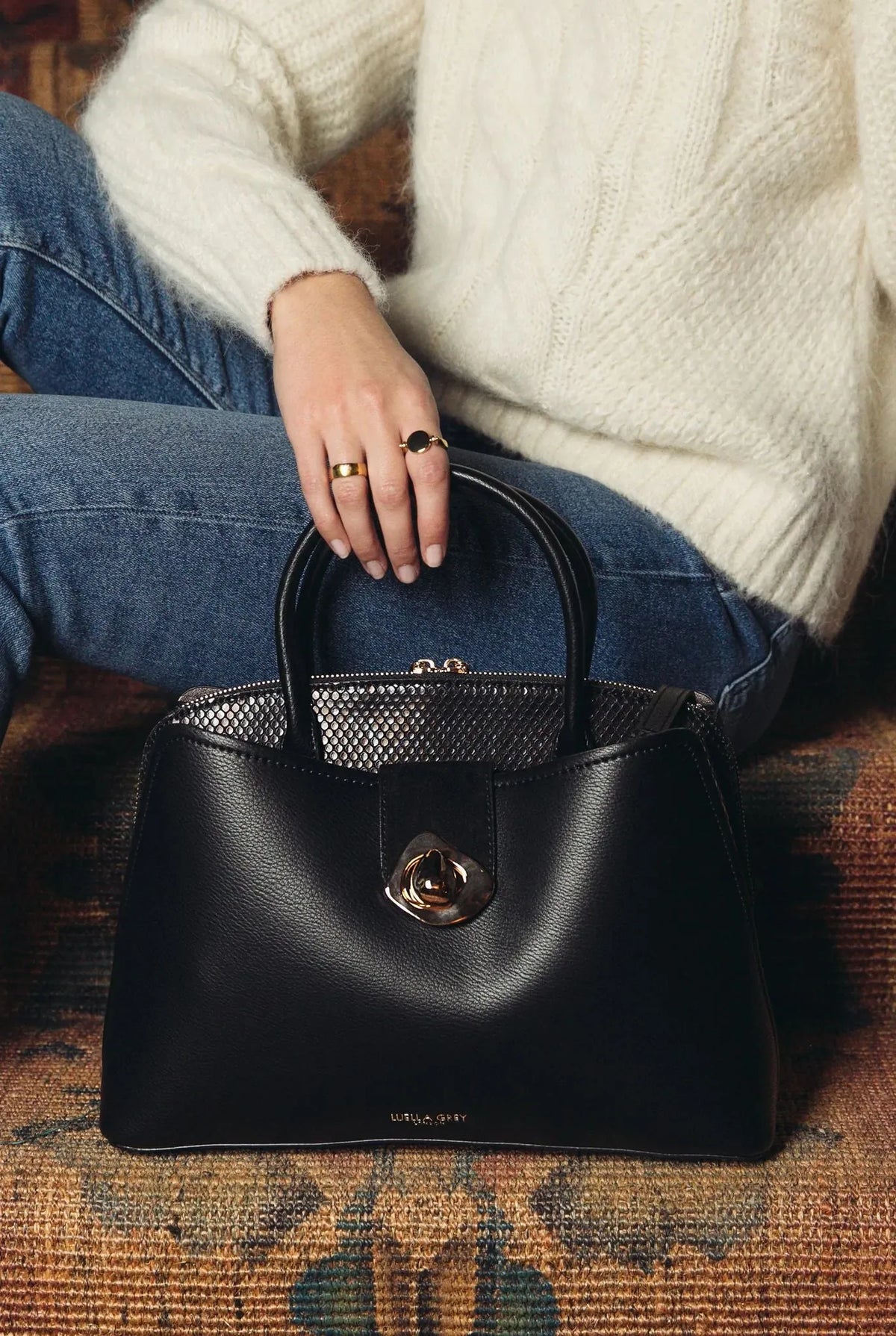 Black handbag with top handles, gold-tone front turn-lock clasp, small mesh panel