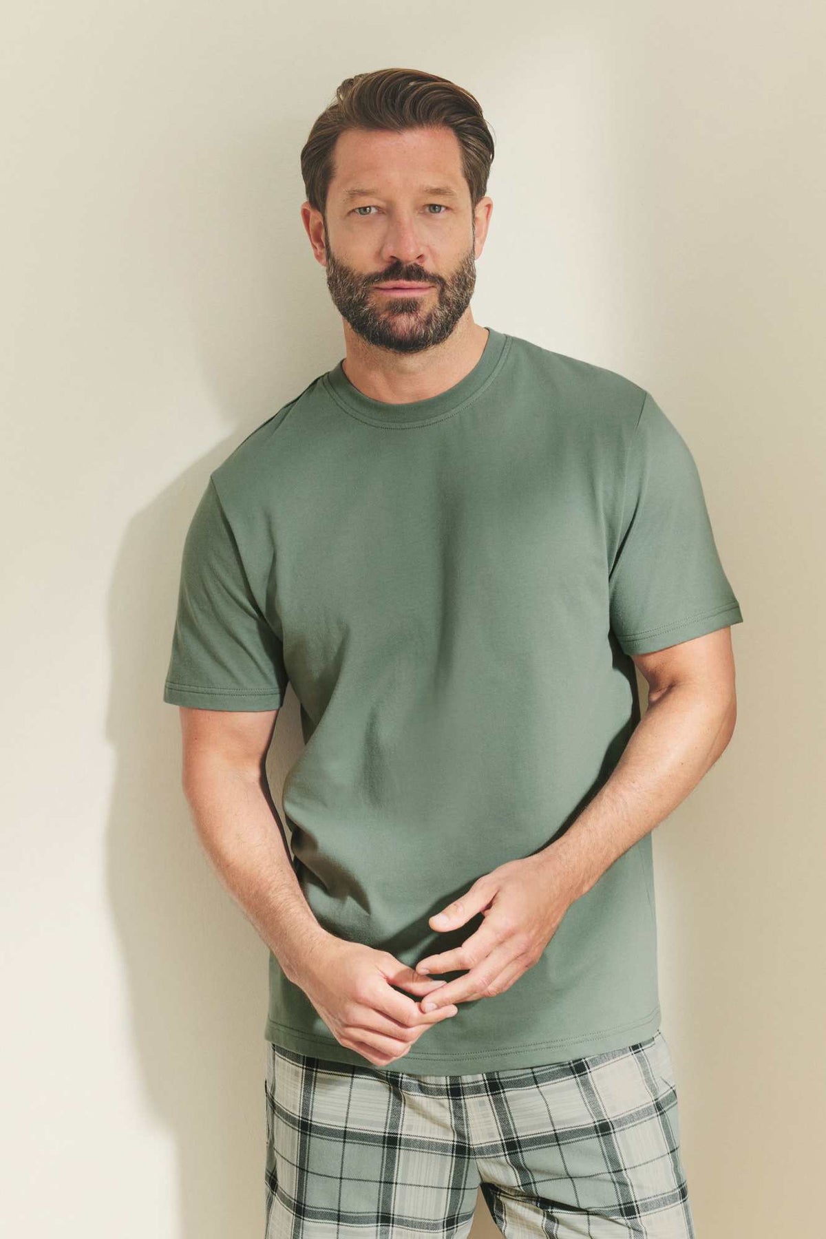 Men's green crewneck T-shirt with plaid drawstring shorts, close-up front view.