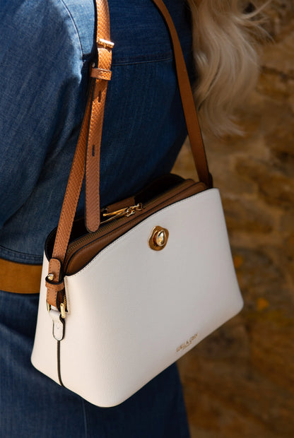 White crossbody handbag close-up with tan strap and gold front clasp