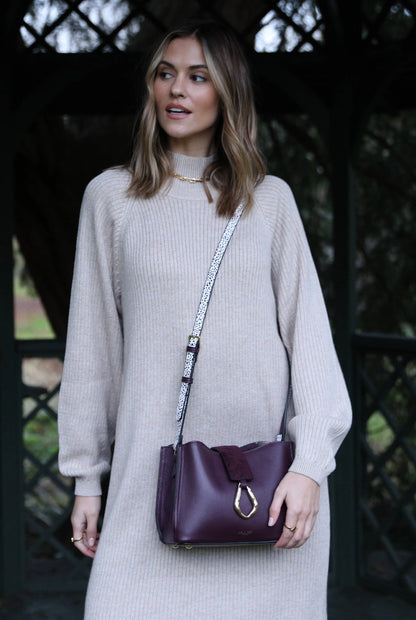 Purple small shoulder bag worn with long strap and front flap clasp