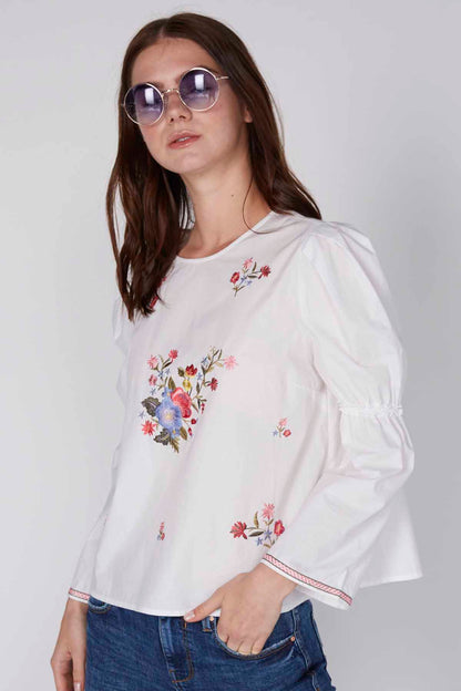 White floral embroidered peasant-style blouse with puff sleeves and ruffled neckline