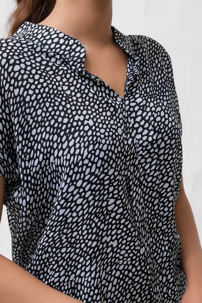 Printed blouse close-up: V-neck collar and curved button placket, black-and-white speckle