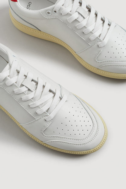 White leather sneakers close-up with perforated toe, laces, and gum sole.
