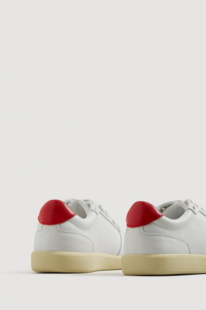 Pair of white low-top sneakers with red heel tabs and gum soles.