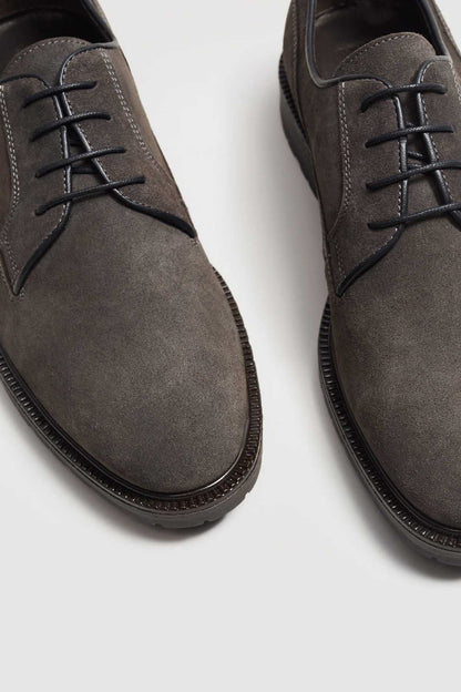 Close-up of grey suede lace-up shoe with black laces and stitched sole edge