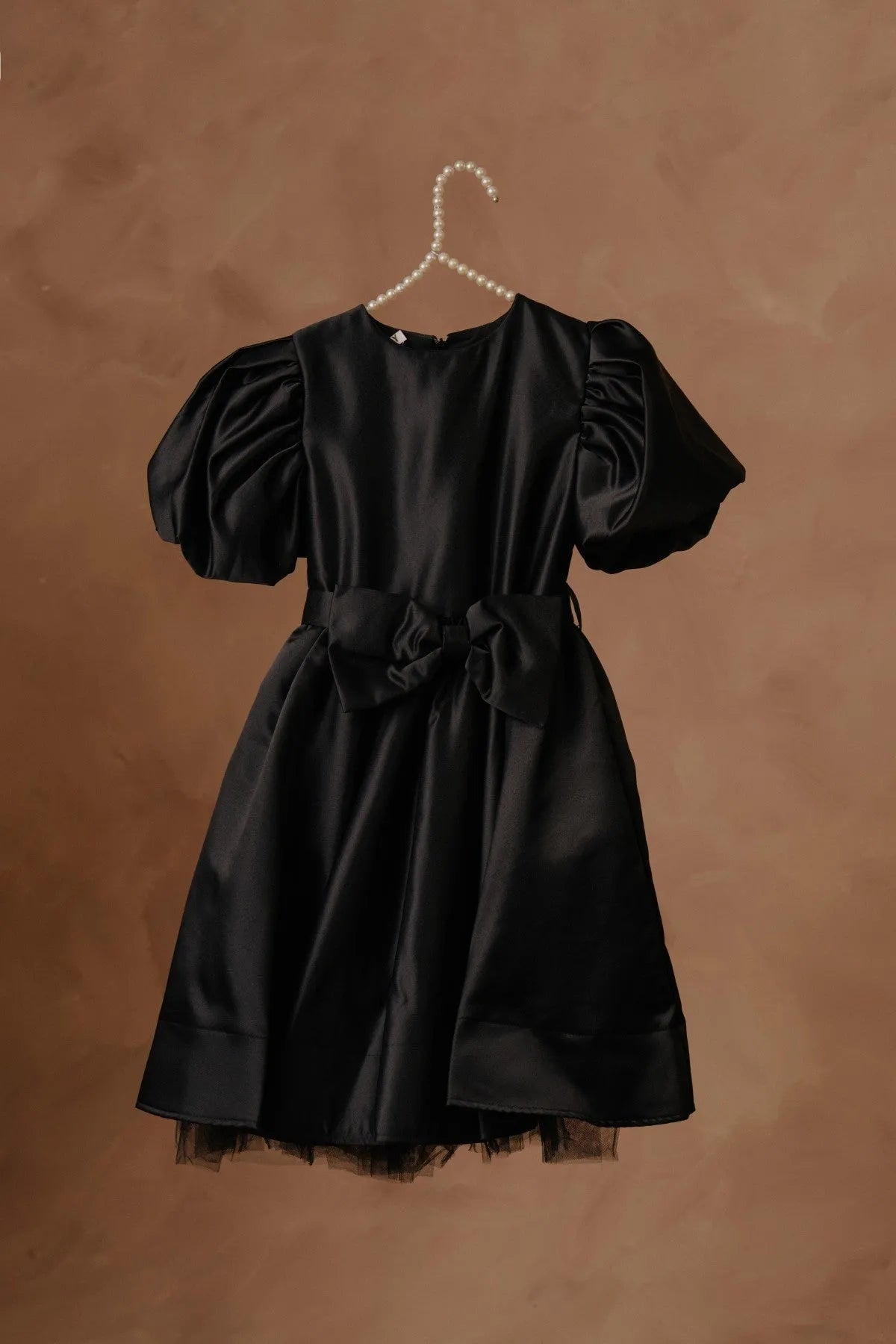 Black puff-sleeve dress with bow waist and tulle-trim hem, on hanger