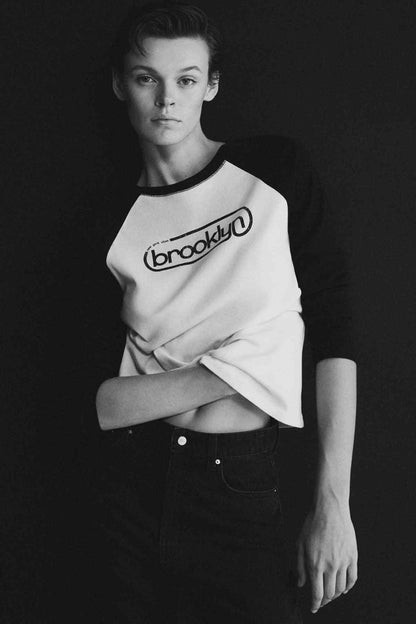 Ecru raglan baseball T-shirt with black sleeves and “brooklyn” logo, upper-body view
