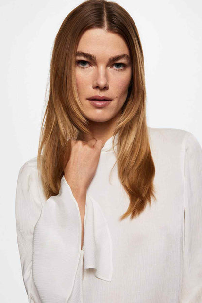Off-white blouse with split V neckline and long sleeves with flared cuff detailing.