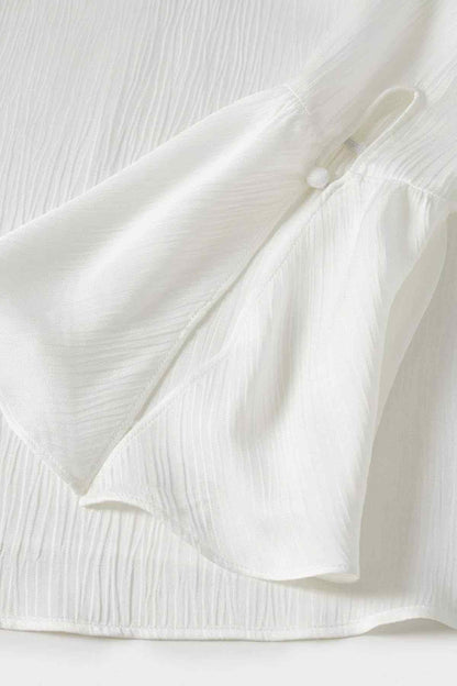 Off-white textured blouse fabric with gathered sleeve cuffs and small button placket.