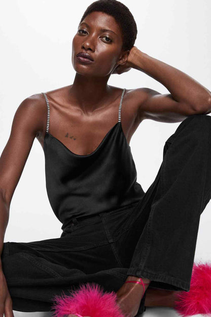 Black satin camisole top with chain straps, layered with black jeans