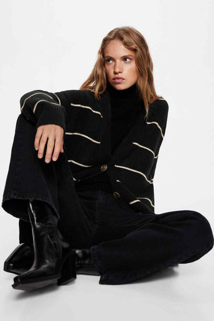 Black striped knit cardigan with button front and long sleeves, model seated