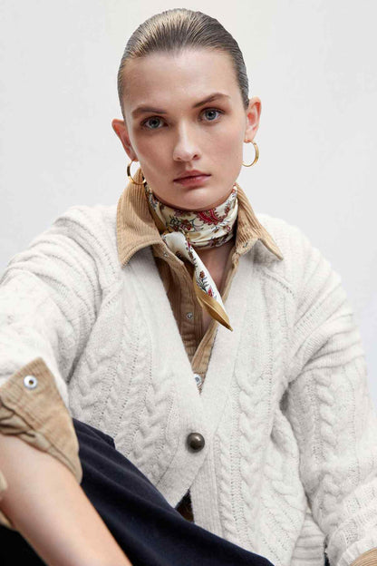 Ecru cable-knit cardigan with tan collar lining and metal button details