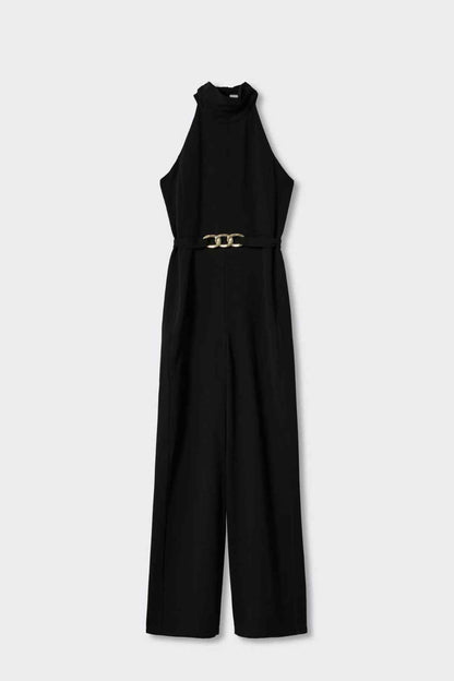 Black sleeveless halter jumpsuit with long neckline tie and gold chain-link belt, wide leg.