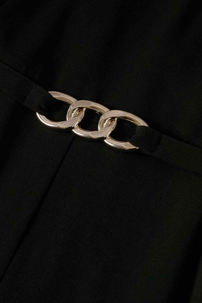 Gold chain-link belt on black jumpsuit waist, centered on front seam.