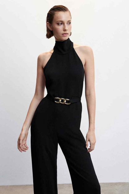 Black halter jumpsuit with high neck and gold chain-link belt, wide-leg pants.