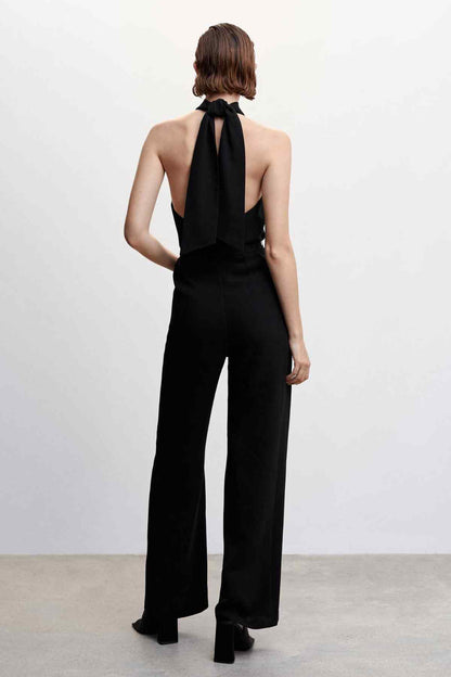 Black halter jumpsuit with long back tie and gold chain-link belt, wide-leg pants.
