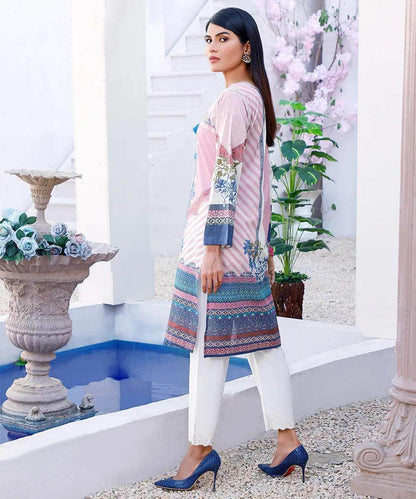 Pastel pink embroidered tunic with blue border, side view over white pants and blue heels
