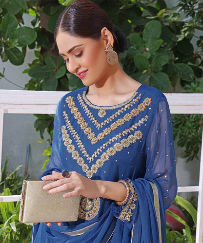 Blue embroidered neckline kurta with gold cuffs and bracelet, clutch in hand