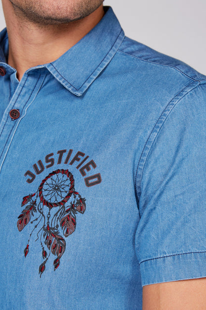 Blue denim short-sleeve button-up with dreamcatcher-style chest embroidery, close-up