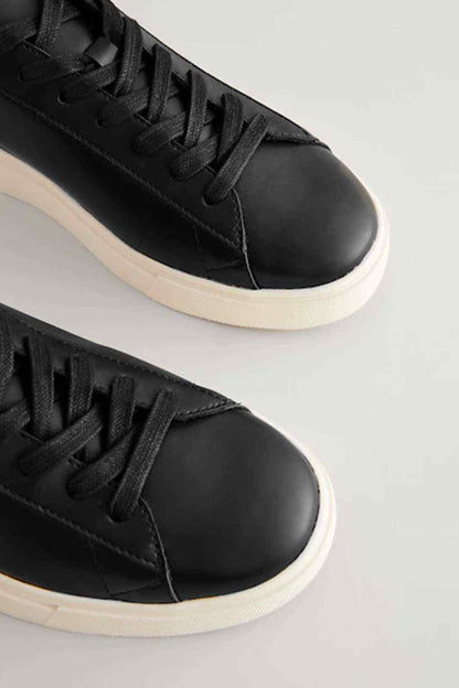 Black lace-up sneakers close-up, black uppers with textured stitching and white sole