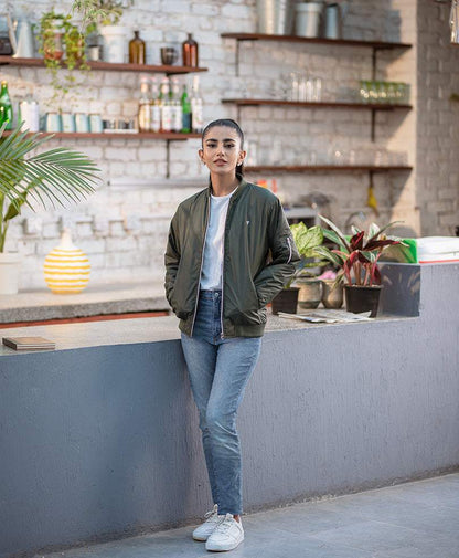 Fitted olive green bomber jacket worn over a light shirt and jeans