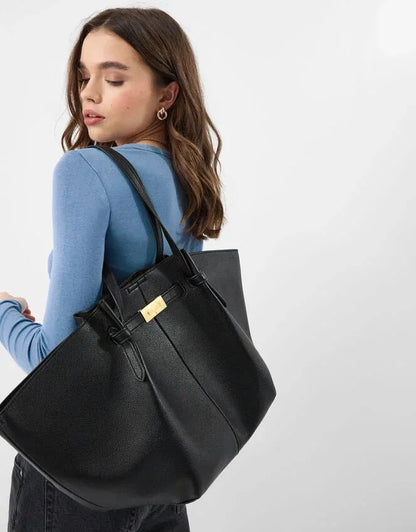 Black tote bag worn over shoulder with gold clasp and stitched panel
