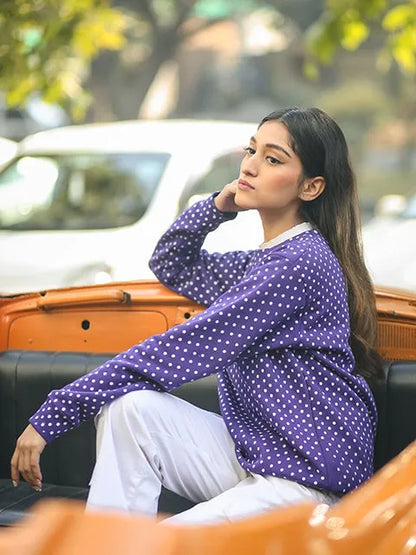 Purple polka-dot long-sleeve top with white crew neck, seated side view