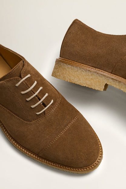 Close-up of dark brown suede lace-up shoe with white laces and tan sole edge