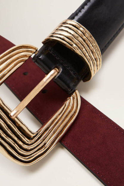 Gold-tone buckle detail on black leather belt with maroon strap lining