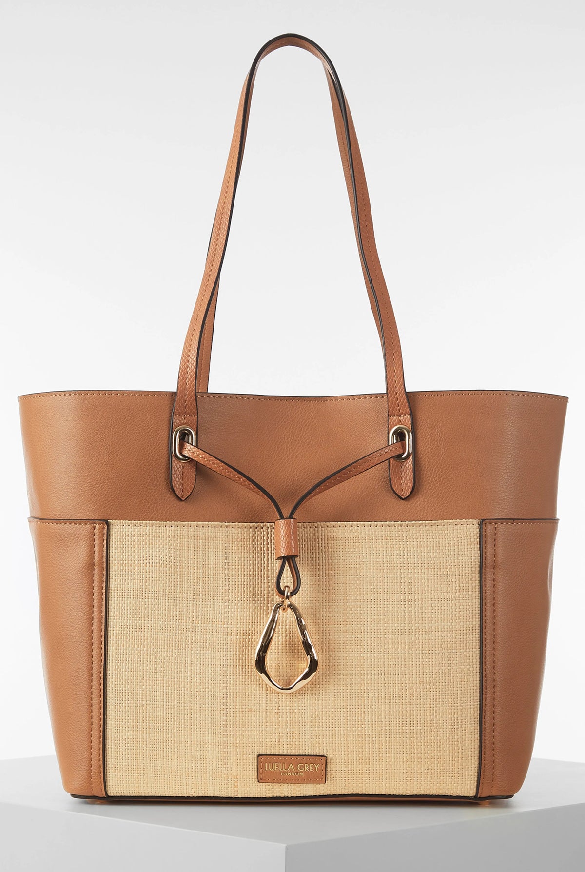 Brown leather-trim woven tote bag with top handles and center teardrop charm
