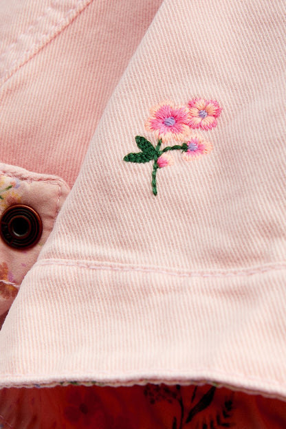 Pink denim jacket close-up with flower embroidery and button detail