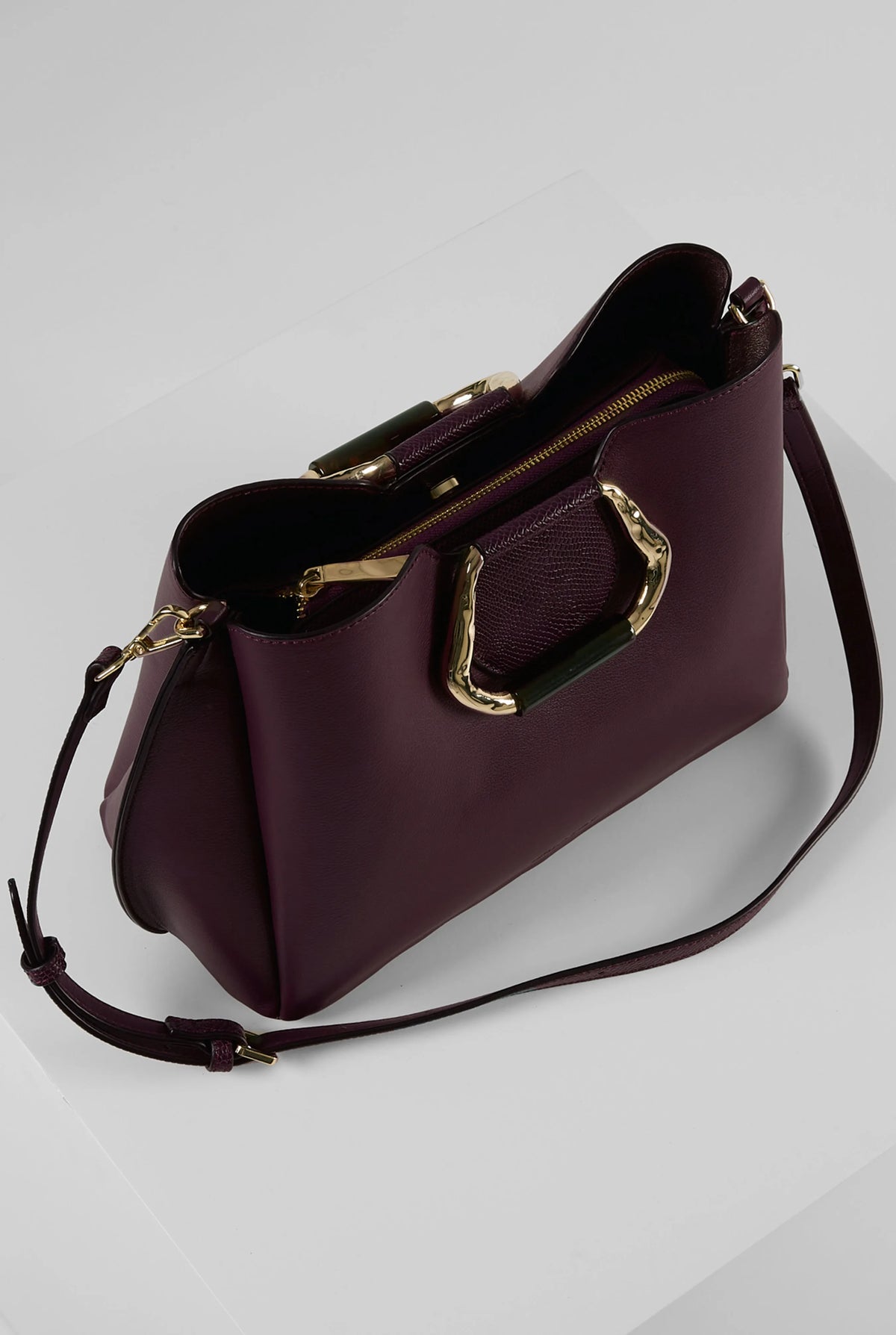 Dark purple handbag angled view with top handle, front flap pocket, and strap
