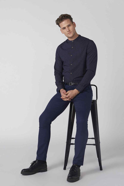 Men's navy patterned button-up shirt and dark blue trousers, seated side view